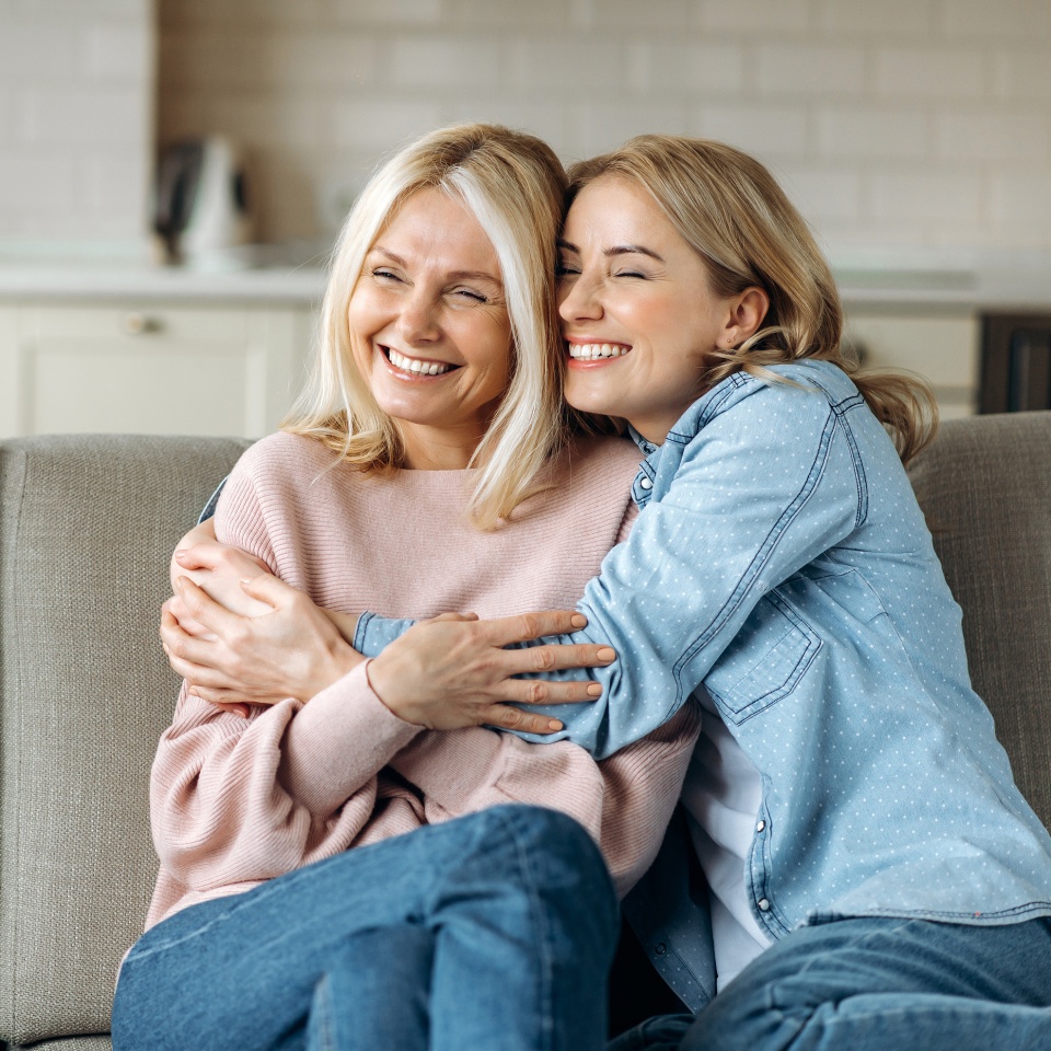 Portrait of caucasian mother and daughter. Mature attractive mother and her young adult happy daughter, are sitting at home on the couch, embracing, smiling. Family values