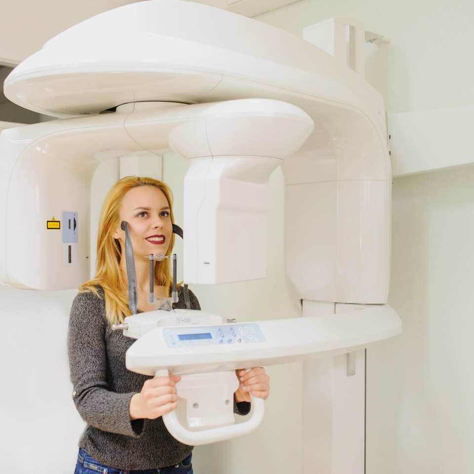 Young woman in a dental 3D x-ray digital scanner panorama machine in clinic.