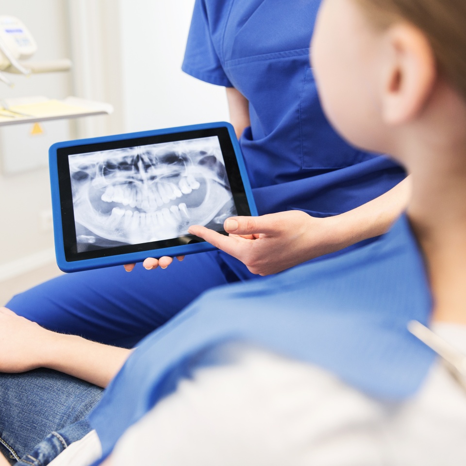 people, medicine, stomatology, technology and health care concept - close up of female dentist showing teeth x-ray on tablet pc computer screen to patient girl at dental clinic office
