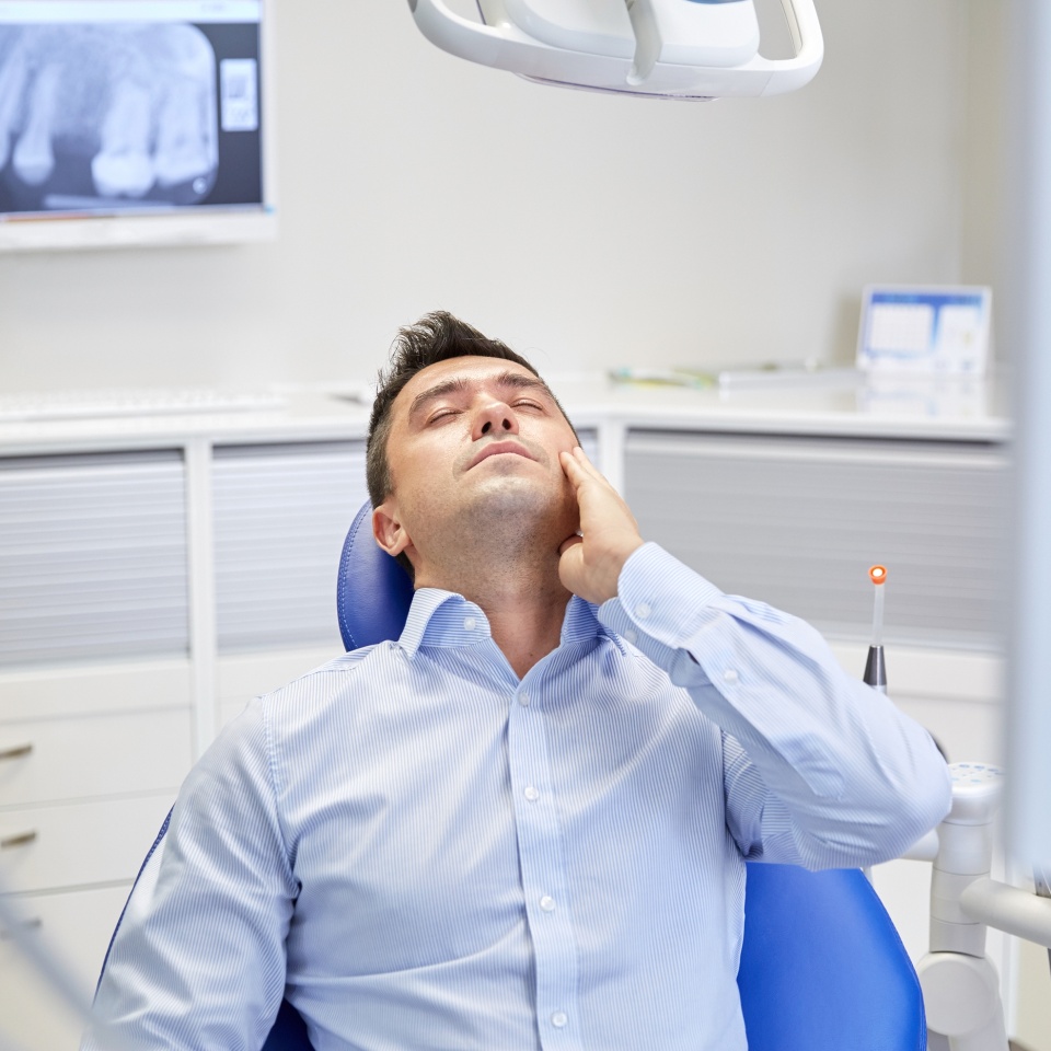 people, medicine, stomatology and health care concept - unhappy male patient having toothache sitting on dental chair at clinic office