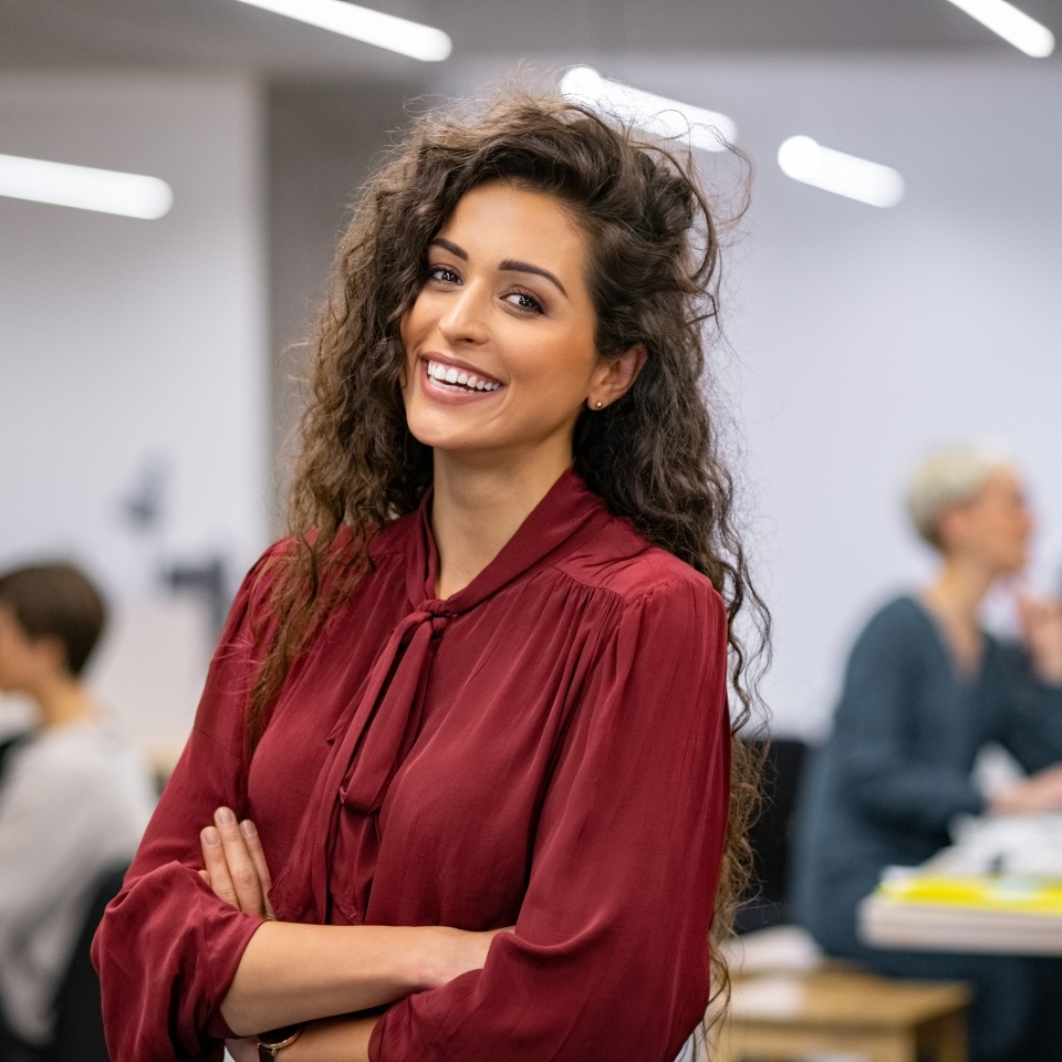 Successful businesswoman standing in creative office and looking at camera while smiling. Portrait of beautiful business woman standing in front of business team at modern agency with copy space.