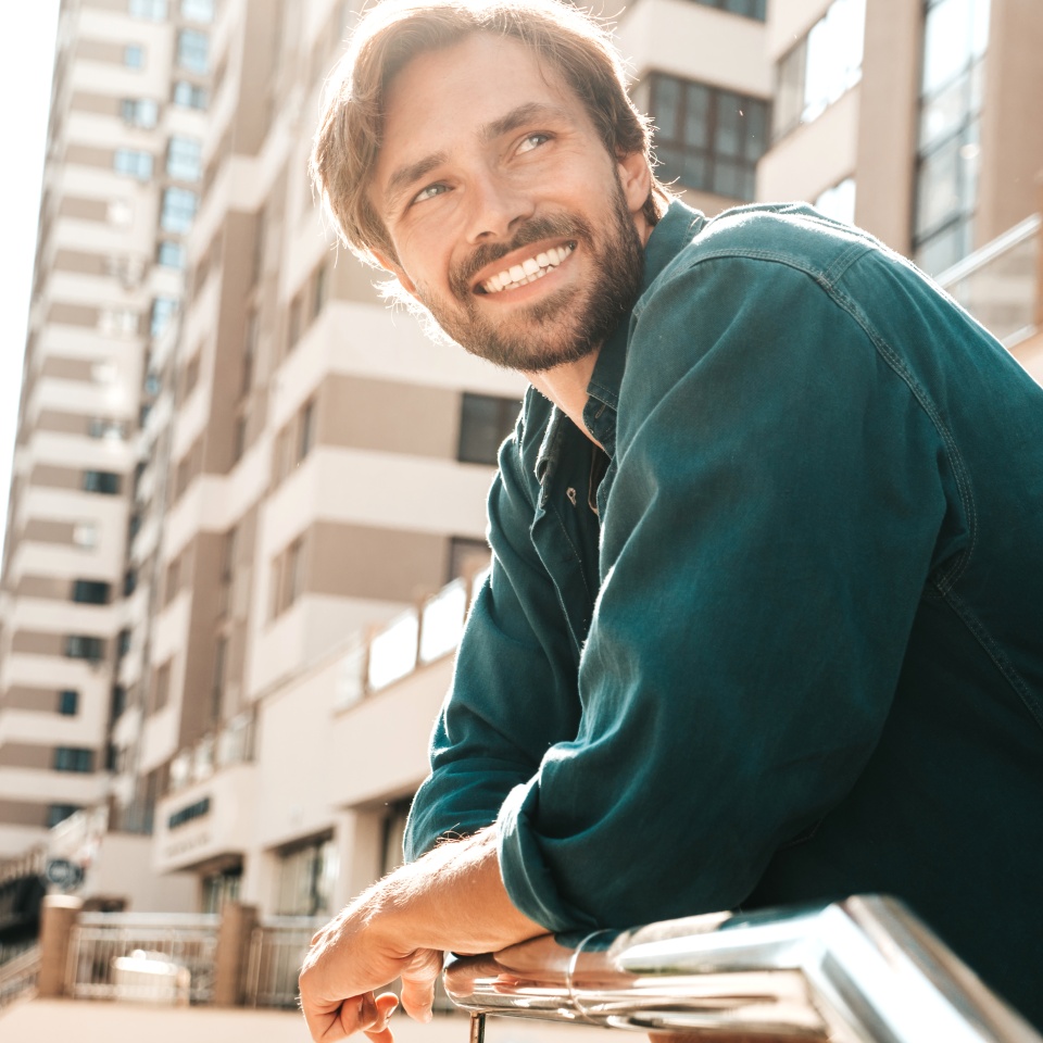 Portrait of handsome smiling stylish hipster lambersexual model.Man dressed in green shirt. Fashion male posing in the street at skyscraper background