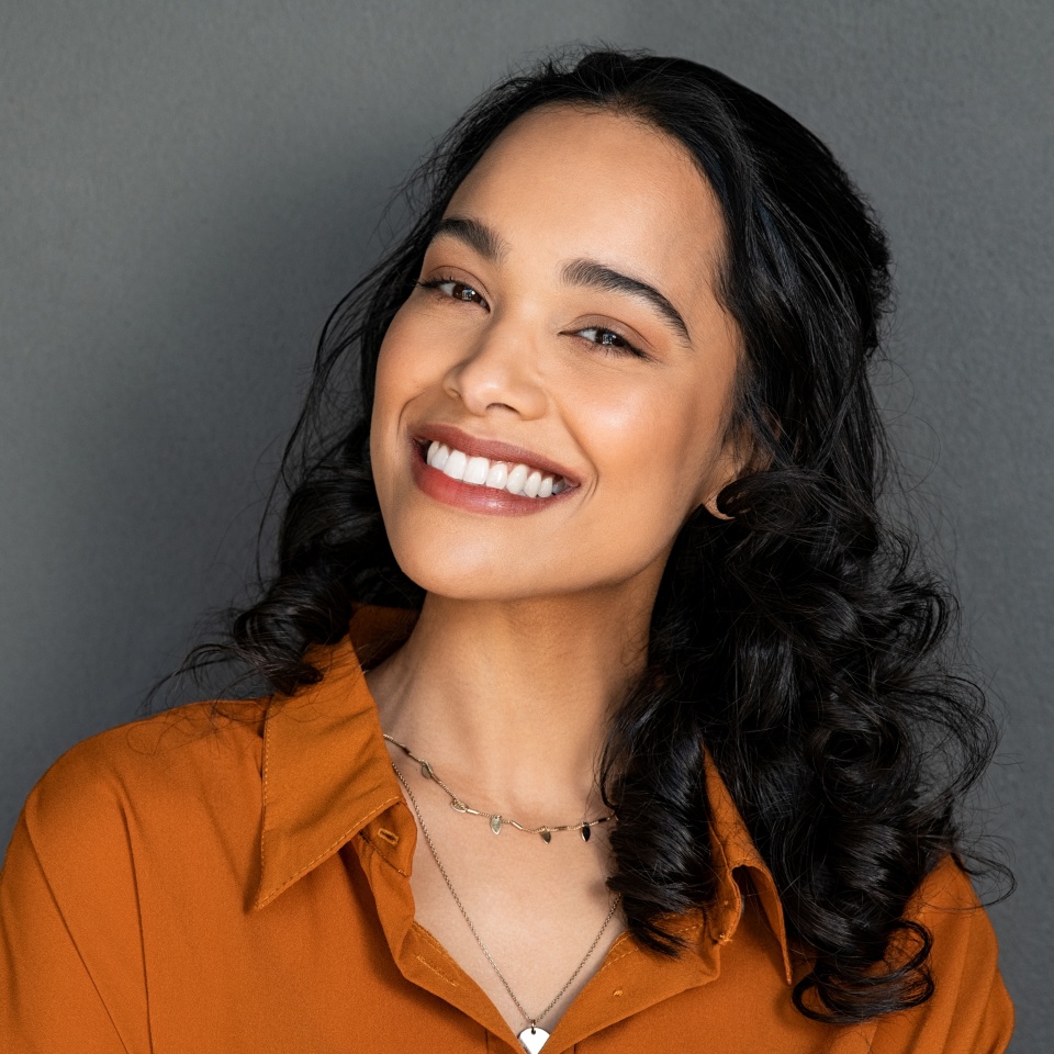 Close up face of young woman with beautiful smile isolated on grey wall with copy space. Successful multiethnic girl. Latin woman looking at camera against gray wall with a big whitening teeth smile.