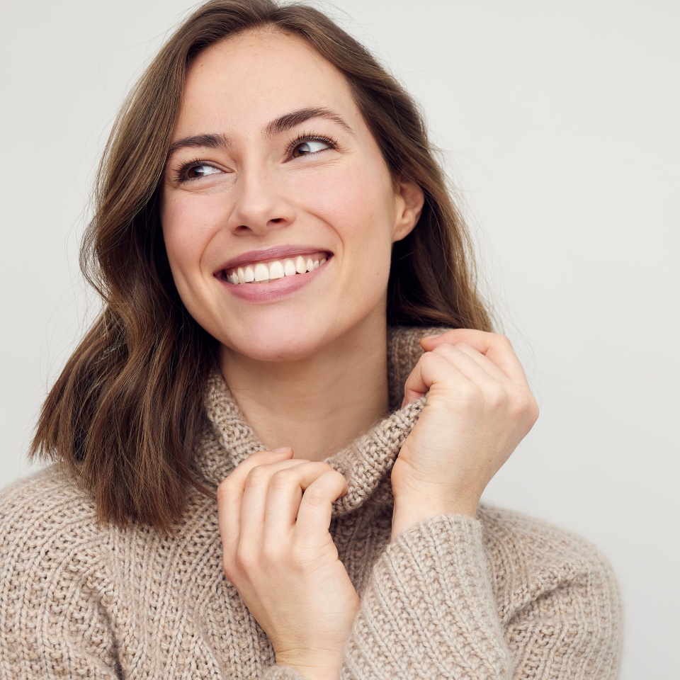 Portrait of young happy woman smiling on white background while looking left. Big smile on her face, looking beautiful, natural and charming.