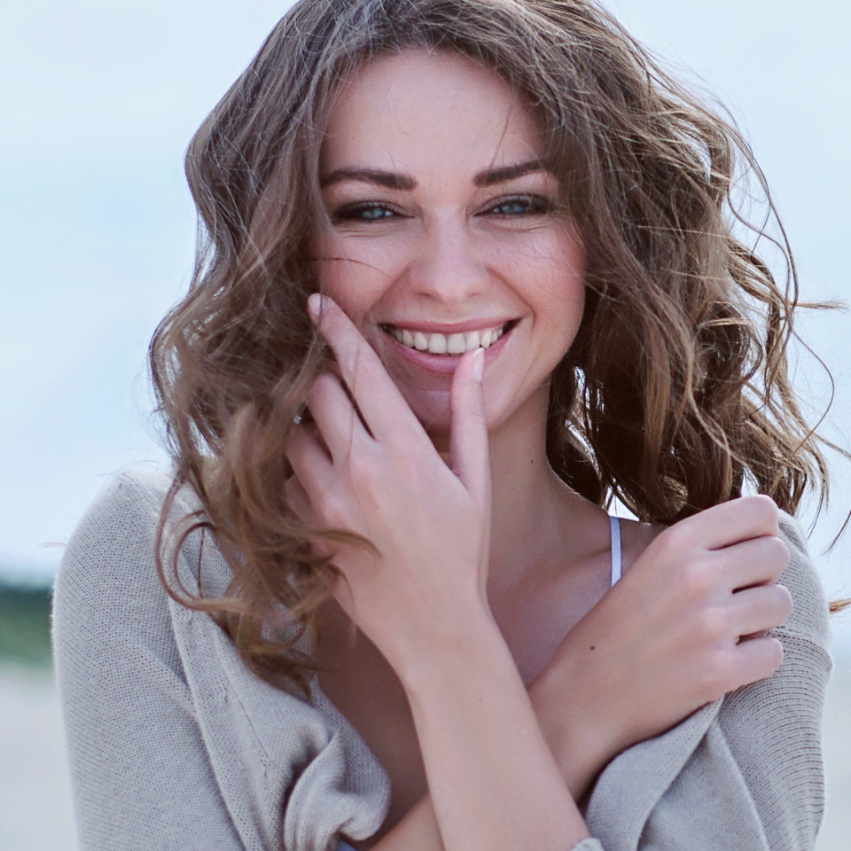 Woman face Portrait on the beach. Happy beautiful curly-haired girl close-up, the wind fluttering hair. Spring portrait on the beach. Young pretty girl. Young smiling outdoors portrait. Close. ocean.
