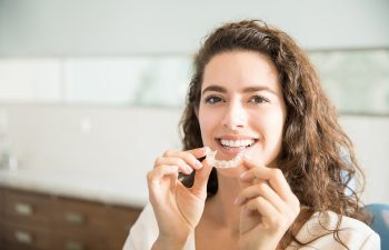 Portrait of beautiful patient holding orthodontic retainers in dental clinic